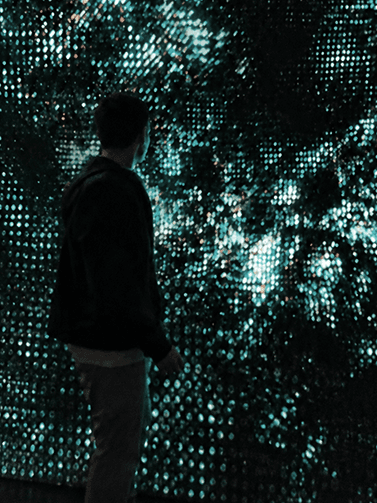 Qussai Khaddour surrounded by turquoise lights in an immersive installation